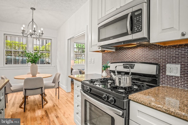 kitchen featuring stone countertops, a notable chandelier, light wood finished floors, decorative backsplash, and appliances with stainless steel finishes