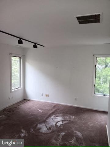 carpeted empty room featuring rail lighting, visible vents, baseboards, and a healthy amount of sunlight