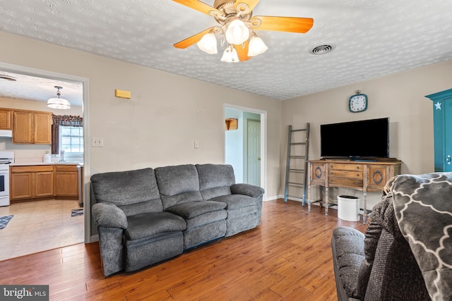 10257 Back Creek Valley Rd, Hedgesville, WV 25427 - living area with a textured ceiling, light wood-type flooring, baseboards, visible vents, and ceiling fan