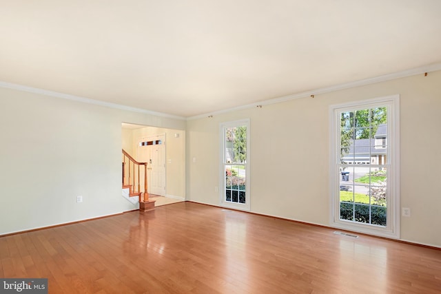 empty room with wood finished floors, visible vents, stairs, and ornamental molding