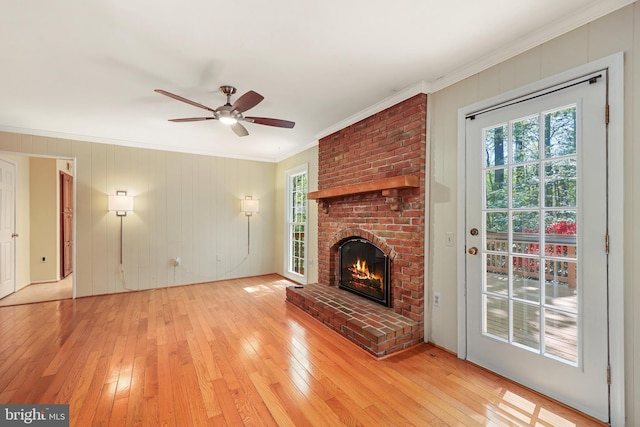 unfurnished living room featuring a ceiling fan, ornamental molding, a brick fireplace, and light wood-type flooring