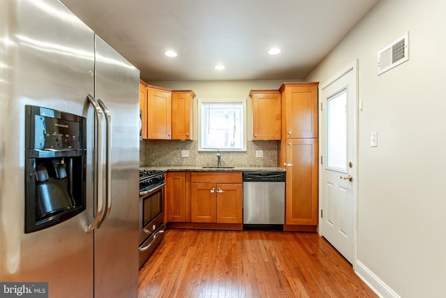 kitchen with visible vents, a sink, light wood finished floors, stainless steel appliances, and stone counters
