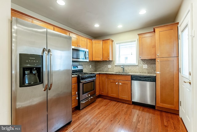 kitchen with tasteful backsplash, light wood-type flooring, light stone counters, stainless steel appliances, and a sink