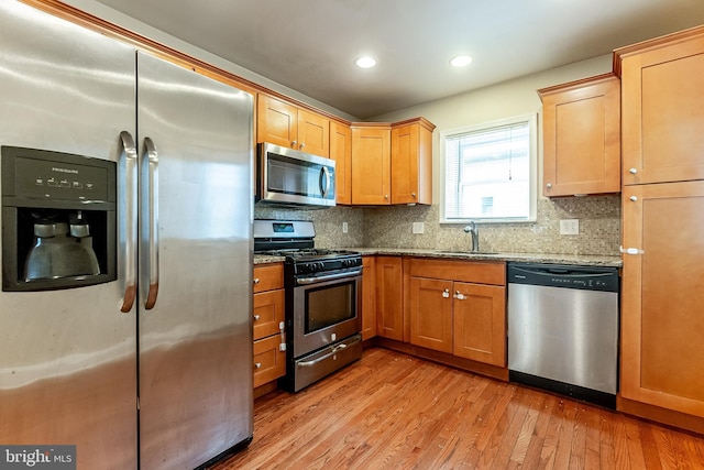 kitchen featuring tasteful backsplash, a sink, light wood finished floors, stainless steel appliances, and light stone counters