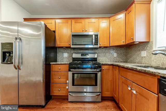 kitchen featuring light stone countertops, light wood-type flooring, a sink, and appliances with stainless steel finishes