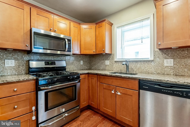 kitchen featuring a sink, brown cabinets, wood finished floors, light stone countertops, and stainless steel appliances