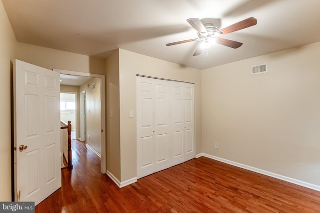 unfurnished bedroom with a closet, a ceiling fan, visible vents, wood finished floors, and baseboards