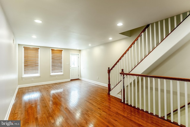 unfurnished living room featuring recessed lighting, hardwood / wood-style flooring, baseboards, and stairs