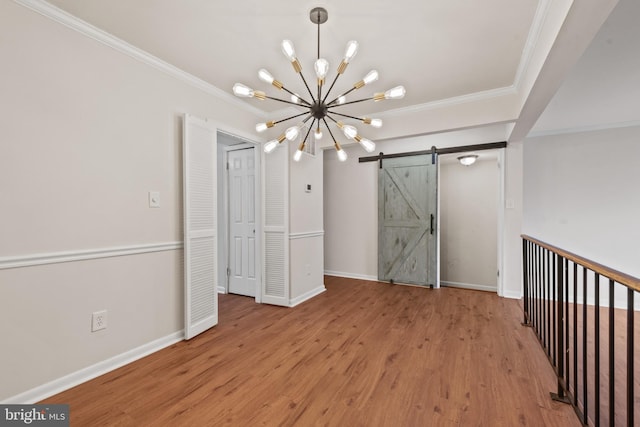empty room with crown molding, a chandelier, a barn door, baseboards, and wood finished floors