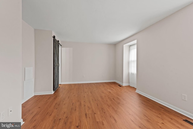 empty room featuring visible vents, baseboards, a barn door, and light wood-style floors