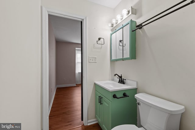 bathroom featuring baseboards, wood finished floors, toilet, and vanity