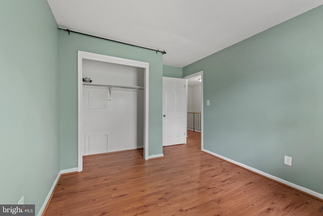 unfurnished bedroom featuring baseboards, wood finished floors, and a closet