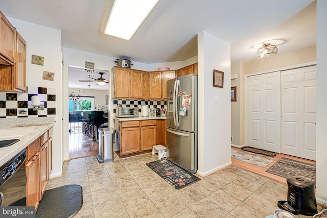 kitchen featuring stainless steel fridge, backsplash, black dishwasher, brown cabinets, and baseboards