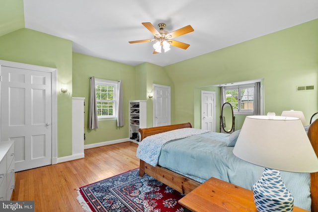 bedroom featuring lofted ceiling, light wood-type flooring, multiple windows, baseboards, and a ceiling fan