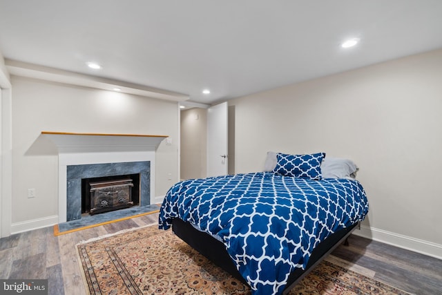 bedroom featuring wood finished floors, a fireplace, recessed lighting, and baseboards