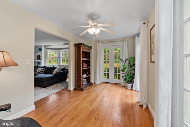 living area featuring light wood-type flooring, ceiling fan, baseboards, and plenty of natural light