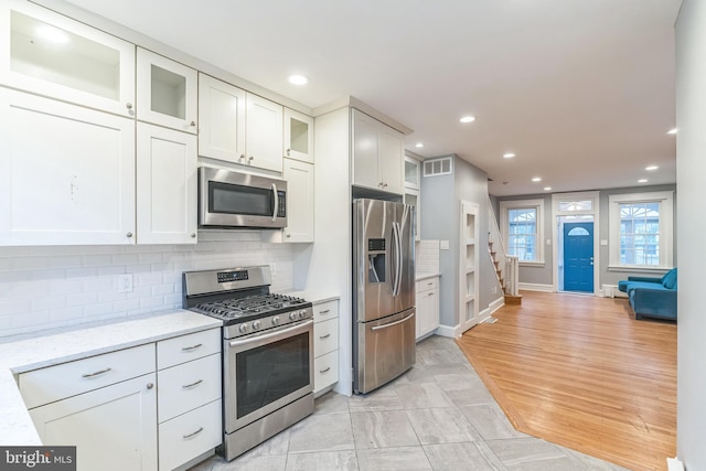 kitchen with light stone counters, visible vents, decorative backsplash, glass insert cabinets, and appliances with stainless steel finishes