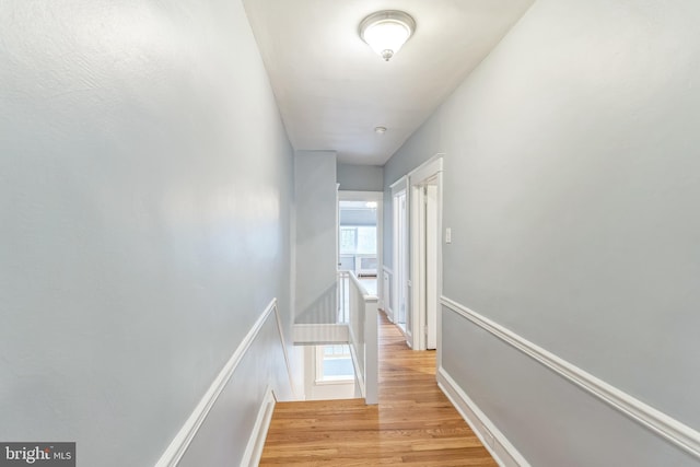 hallway featuring light wood finished floors, baseboards, and an upstairs landing