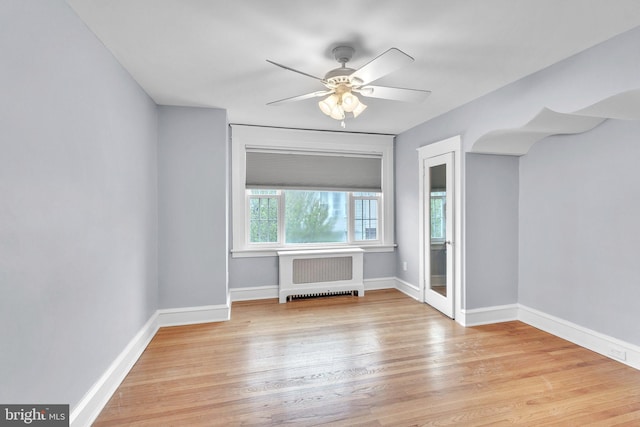 spare room featuring radiator, baseboards, a ceiling fan, and light wood finished floors