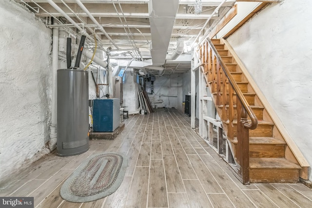 unfinished below grade area featuring heating unit, water heater, wood finished floors, and stairs
