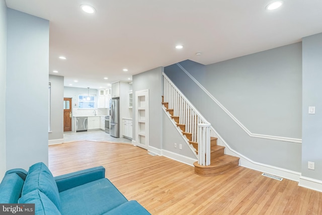 living room with light wood-style flooring, baseboards, visible vents, recessed lighting, and stairway
