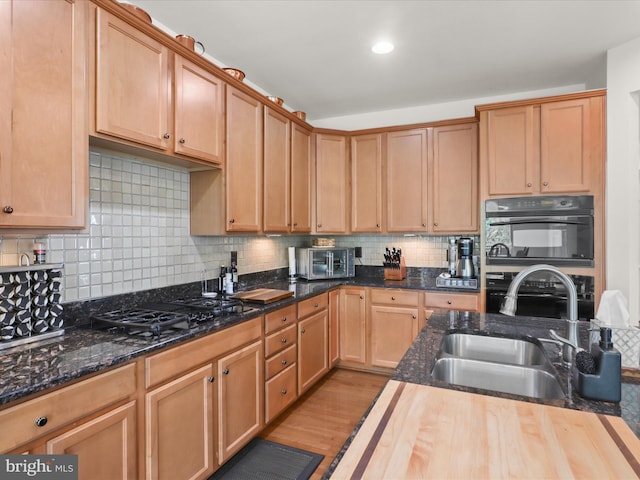 kitchen featuring dark stone counters, decorative backsplash, a sink, a toaster, and light wood-type flooring