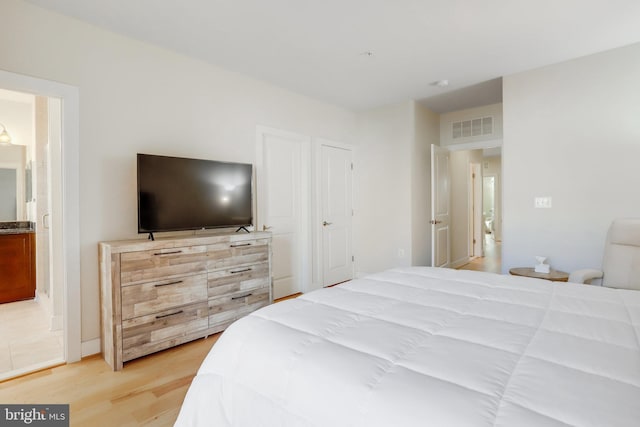 bedroom featuring light wood-type flooring, ensuite bath, and visible vents