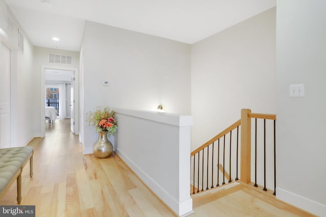 hall with visible vents, baseboards, wood finished floors, and an upstairs landing