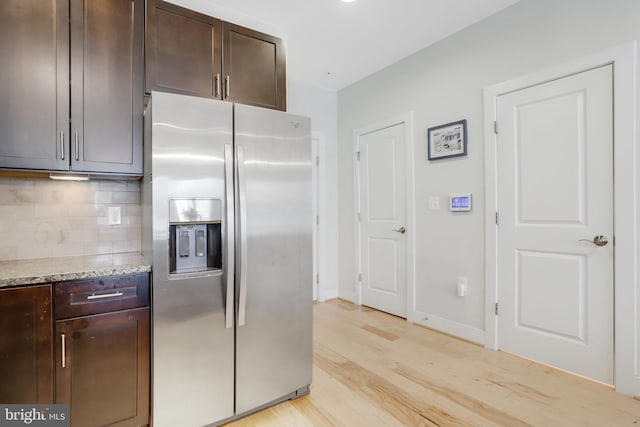 kitchen featuring decorative backsplash, dark brown cabinetry, stainless steel fridge with ice dispenser, light stone counters, and light wood finished floors