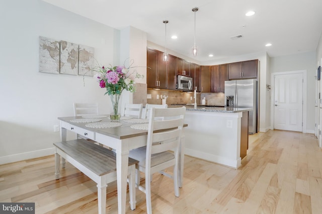 kitchen with light wood finished floors, stainless steel appliances, baseboards, a peninsula, and decorative backsplash