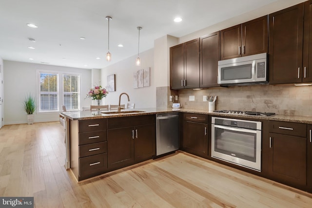 kitchen featuring dark brown cabinets, appliances with stainless steel finishes, a sink, a peninsula, and light wood-type flooring