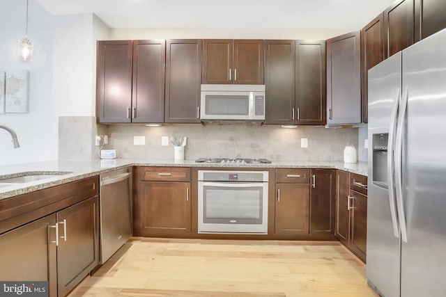 kitchen featuring a sink, appliances with stainless steel finishes, backsplash, and light wood finished floors