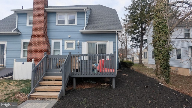 rear view of property featuring a chimney, a wooden deck, and roof with shingles