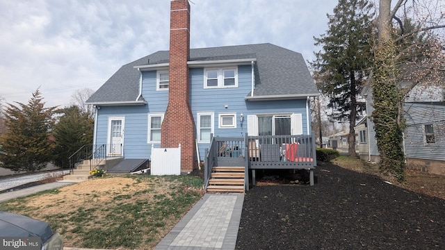 back of house featuring a chimney, a shingled roof, and a wooden deck