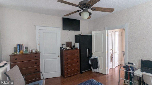 bedroom featuring a textured wall, ceiling fan, and dark wood-style flooring