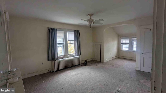 carpeted spare room with arched walkways, ceiling fan, and radiator