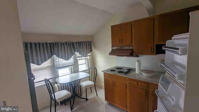 kitchen with light countertops, stainless steel electric stovetop, under cabinet range hood, brown cabinetry, and vaulted ceiling
