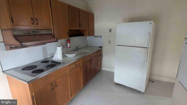 kitchen with baseboards, a sink, light countertops, freestanding refrigerator, and stainless steel electric cooktop