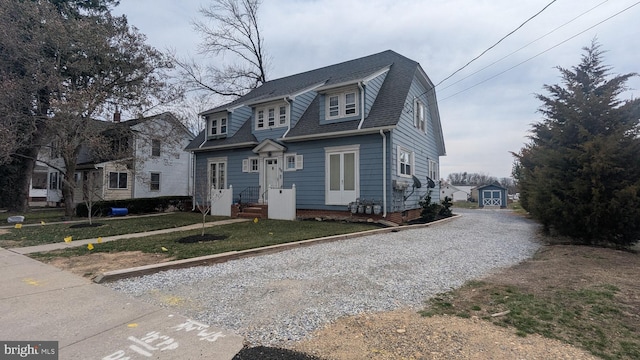 view of front of property with a gambrel roof, an outdoor structure, gravel driveway, a front lawn, and a shingled roof