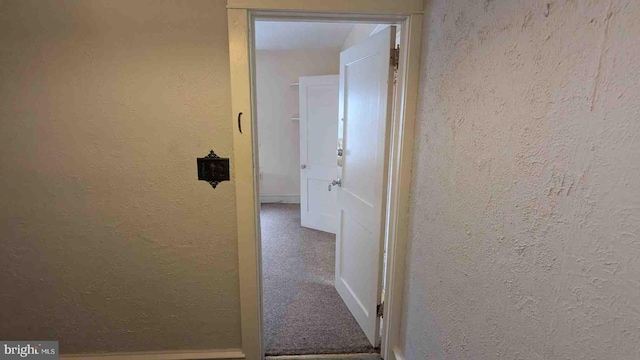 hallway with a textured wall, baseboards, and carpet floors