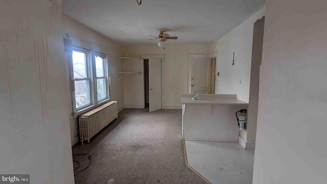 interior space featuring light colored carpet, radiator, ceiling fan, and baseboards