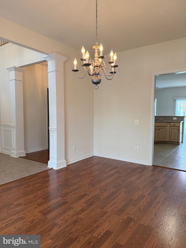unfurnished dining area with baseboards, dark wood finished floors, a notable chandelier, and decorative columns