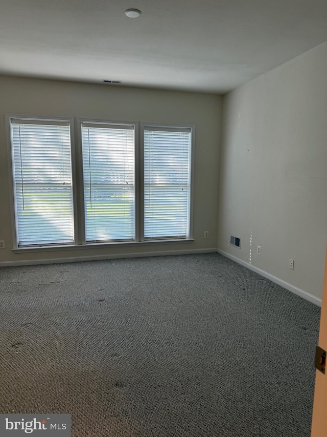 carpeted empty room with baseboards, a wealth of natural light, and visible vents