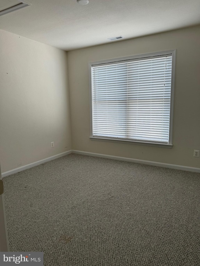carpeted empty room with baseboards, a wealth of natural light, and visible vents