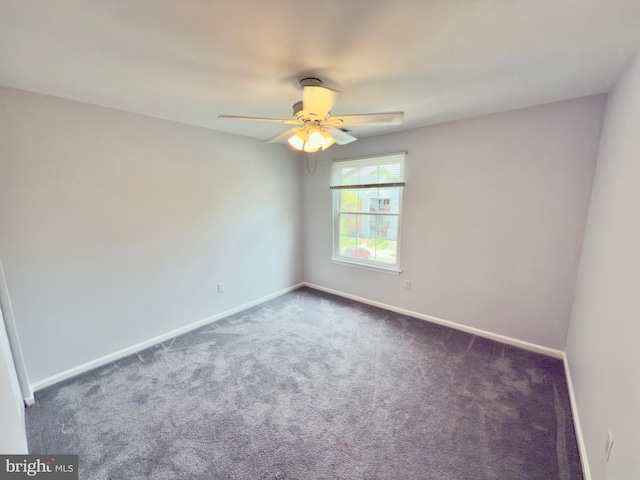 spare room with dark colored carpet, a ceiling fan, and baseboards