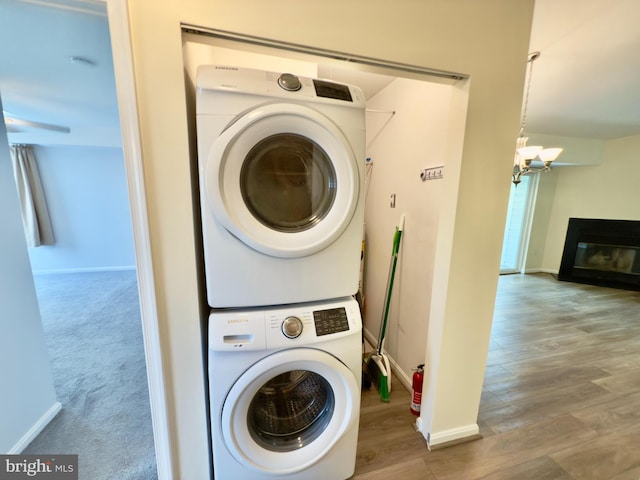 washroom featuring a glass covered fireplace, baseboards, a chandelier, stacked washer / drying machine, and laundry area