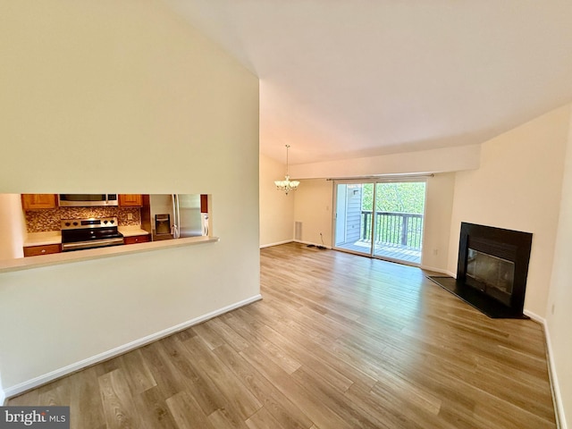 unfurnished living room with lofted ceiling, a glass covered fireplace, light wood-type flooring, baseboards, and a notable chandelier