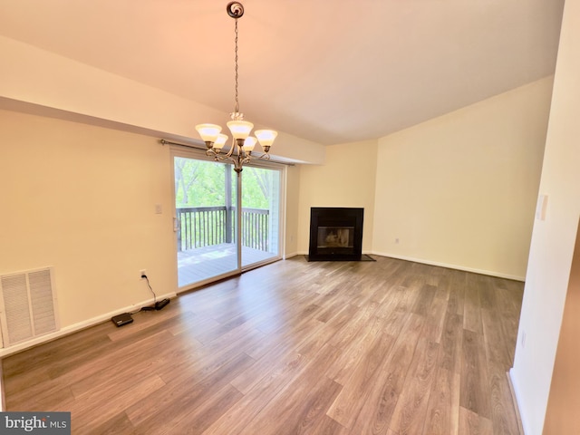 unfurnished living room with baseboards, wood finished floors, visible vents, and a notable chandelier