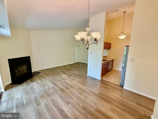 unfurnished living room with a glass covered fireplace, an inviting chandelier, light wood-style flooring, baseboards, and visible vents