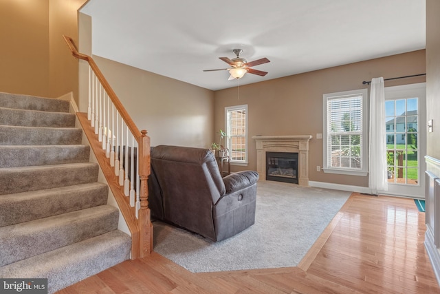 living room with a healthy amount of sunlight, ceiling fan, a glass covered fireplace, and stairs